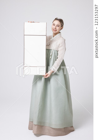 A Western woman standing wearing a Hanbok and holding a hanging scroll 123153297