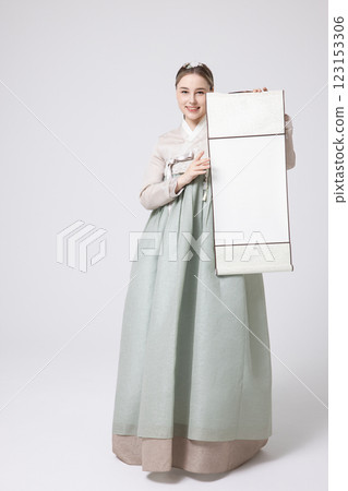 A Western woman standing wearing a Hanbok and holding a hanging scroll 123153306