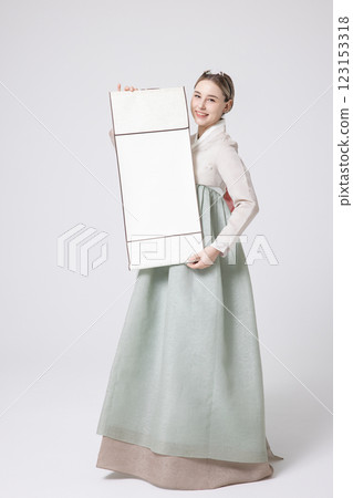 A Western woman standing wearing a Hanbok and holding a hanging scroll 123153318