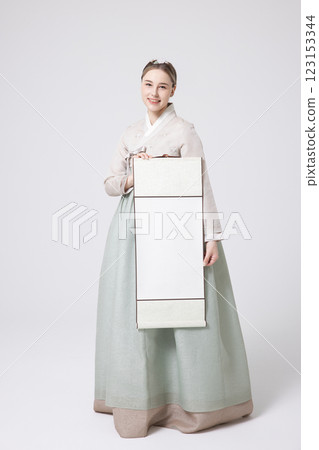A Western woman standing wearing a Hanbok and holding a hanging scroll 123153344