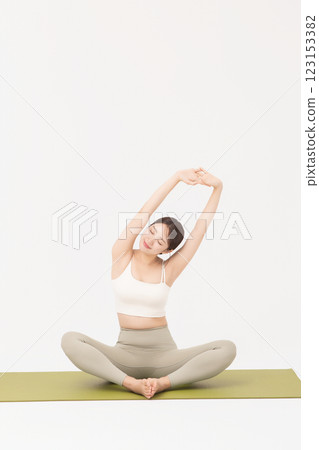 Portrait of a young woman wearing sportswear sitting on a yoga mat and stretching Portrait of a young woman wearing sportswear sitting on a yoga mat and stretching 123153382