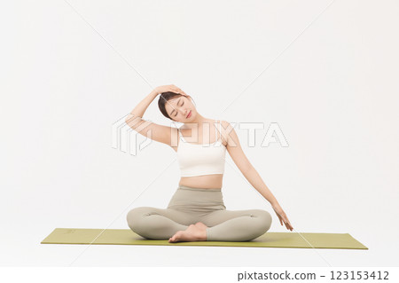 Portrait of a young woman wearing sportswear sitting on a yoga mat and stretching 123153412