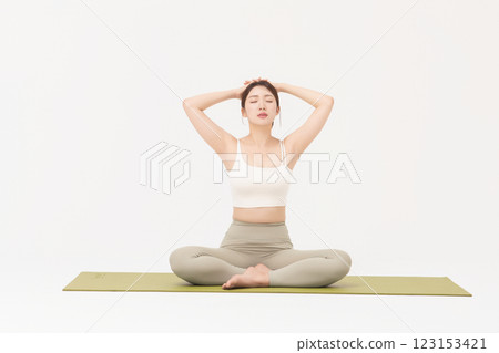 Portrait of a young woman wearing sportswear sitting on a yoga mat and stretching 123153421