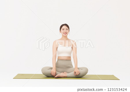 Portrait of a young woman wearing sportswear sitting on a yoga mat and stretching 123153424