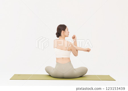 Portrait of a young woman wearing sportswear sitting on a yoga mat and stretching 123153439
