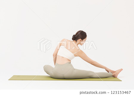 Portrait of a young woman wearing sportswear sitting on a yoga mat and stretching Portrait of a young woman wearing sportswear sitting on a yoga mat and stretching 123153467