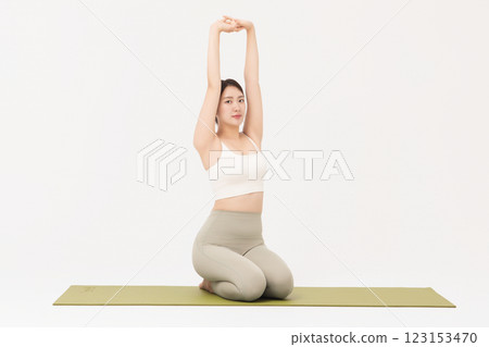 Portrait of a young woman wearing sportswear sitting on a yoga mat and stretching 123153470