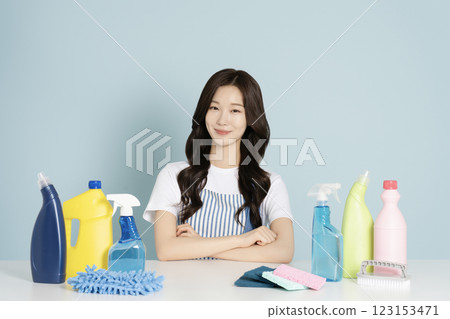 A woman in her 20s sitting in an apron in front of a table with cleaning tools on it 123153471