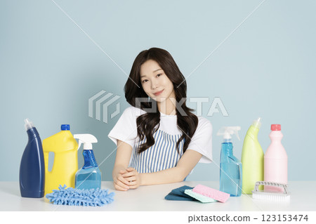 A woman in her 20s sitting in an apron in front of a table with cleaning tools on it 123153474
