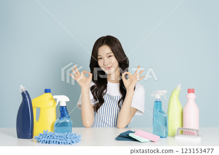 A woman in her 20s sitting in an apron in front of a table with cleaning tools on it 123153477