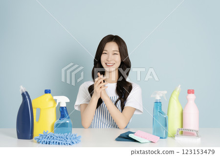 A woman in her 20s sitting in an apron in front of a table with cleaning tools on it A woman in her 20s sitting in an apron in front of a table with cleaning tools on it 123153479