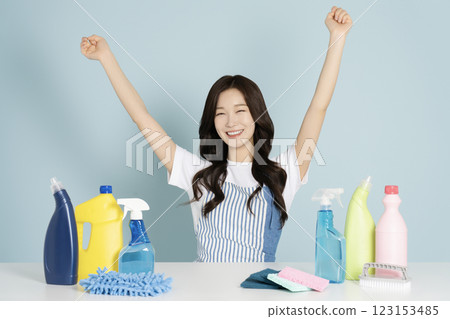 A woman in her 20s sitting in an apron in front of a table with cleaning tools on it A woman in her 20s sitting in an apron in front of a table with cleaning tools on it 123153485
