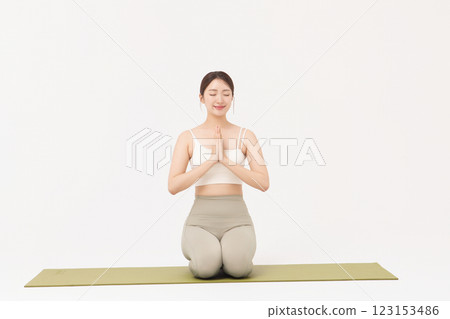 Portrait of a young woman wearing sportswear sitting on a yoga mat and stretching Portrait of a young woman wearing sportswear sitting on a yoga mat and stretching 123153486