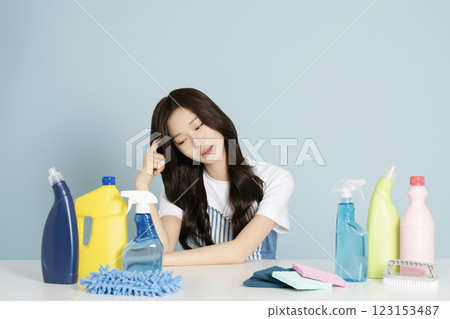 A woman in her 20s sitting in an apron in front of a table with cleaning tools on it A woman in her 20s sitting in an apron in front of a table with cleaning tools on it 123153487