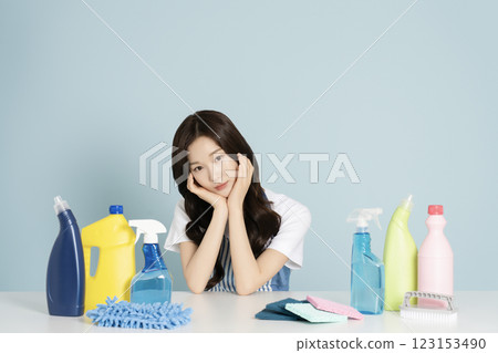A woman in her 20s sitting in an apron in front of a table with cleaning tools on it 123153490