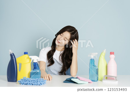 A woman in her 20s sitting in an apron in front of a table with cleaning tools on it 123153493