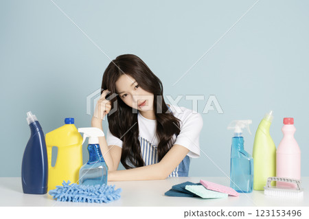 A woman in her 20s sitting in an apron in front of a table with cleaning tools on it 123153496