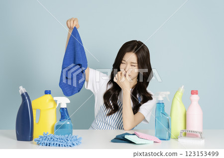 A woman in her 20s sitting in front of a table with cleaning tools, holding a mop and covering her nose A woman in her 20s sitting in front of a table with cleaning tools, holding a mop and covering her nose 123153499