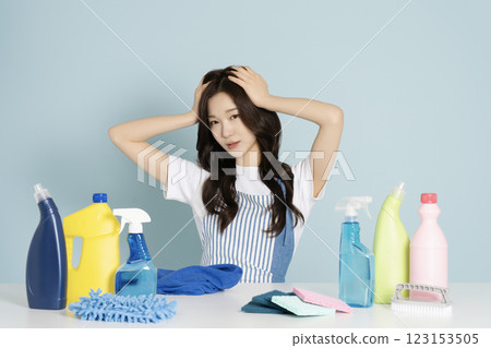 A woman in her 20s suffering from a headache while sitting in front of a table with cleaning tools on it A woman in her 20s suffering from a headache while sitting in front of a table with cleaning tools on it 123153505
