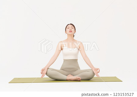 Portrait of a young woman wearing sportswear sitting on a yoga mat and stretching 123153527