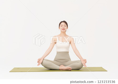 Portrait of a young woman wearing sportswear sitting on a yoga mat and stretching Portrait of a young woman wearing sportswear sitting on a yoga mat and stretching 123153536