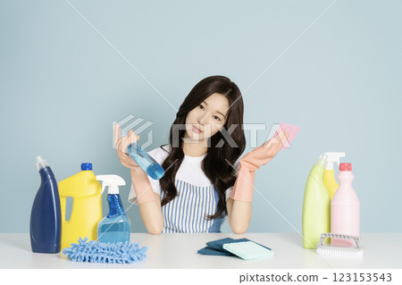 A woman in her 24s sitting in front of a table, wearing rubber gloves and holding a cleaning tool 123153543
