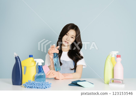 A woman in her 25s sitting in front of a table, wearing rubber gloves and holding a cleaning tool 123153546