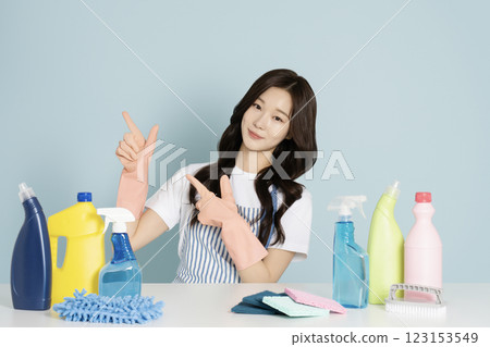A woman in her 20s wearing rubber gloves and an apron sitting in front of a table with cleaning tools on it 123153549