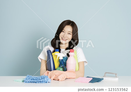 A woman in her 20s sitting in front of a table, wearing rubber gloves and holding a cleaning tool 123153562