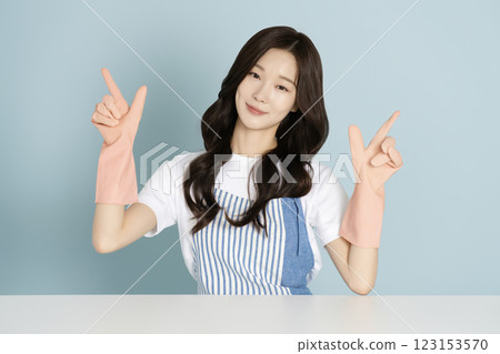 A woman in her 20s sitting in front of a table wearing rubber gloves 123153570