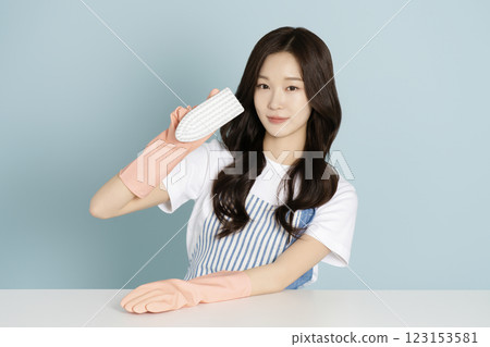 A woman in her 20s sitting in front of a table wearing rubber gloves and wiping the desk 123153581