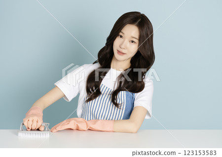 A woman in her 20s sitting in front of a table wearing rubber gloves and wiping the desk 123153583