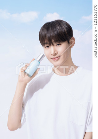 Young man holding basic cosmetics products and standing with clouds in the background 123153770