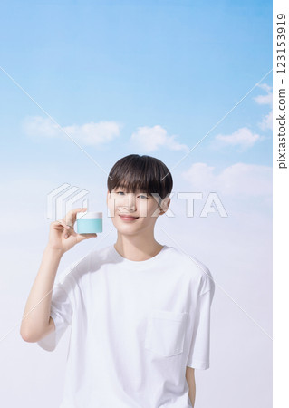 Young man holding basic cosmetics products and standing with clouds in the background Young man holding basic cosmetics products and standing with clouds in the background 123153919