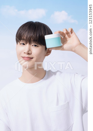 Young man holding basic cosmetics products and standing with clouds in the background 123153945