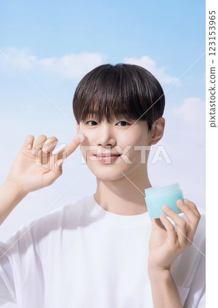 Young man holding basic cosmetics products and standing with clouds in the background 123153965