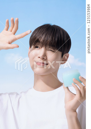 Young man holding basic cosmetics products and standing with clouds in the background 123153984