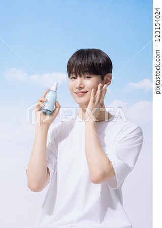 Young man holding basic cosmetics products and standing with clouds in the background 123154024