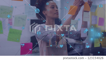 Image of network of media icons over biracial casual businesswoman brainstorming at office Image of network of media icons over biracial casual businesswoman brainstorming at office 123154026
