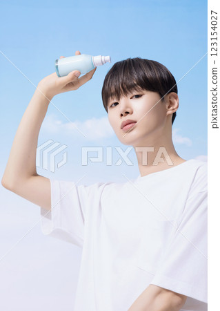 Young man holding basic cosmetics products and standing with clouds in the background Young man holding basic cosmetics products and standing with clouds in the background 123154027