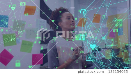 Image of networks of media icons over biracial casual businesswoman brainstorming at office Image of networks of media icons over biracial casual businesswoman brainstorming at office 123154055
