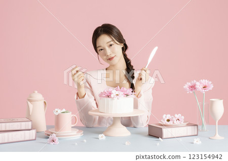 A woman in her 20s sitting in front of a cake holding a fork and knife 123154942