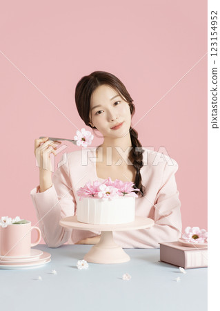 A woman in her 20s sitting in front of a cake and scooping up flowers with a fork. 123154952