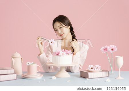 A woman in her 20s sitting in front of a cake and scooping up flowers with a fork. 123154955