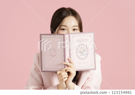 A woman in her 20s holding a pink book and covering her face 123154991