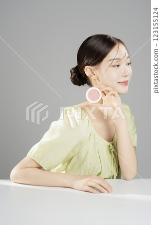 A pretty woman in her 20s wearing bright clothes, sitting and posing with cosmetics A pretty woman in her 20s wearing bright clothes, sitting and posing with cosmetics 123155124