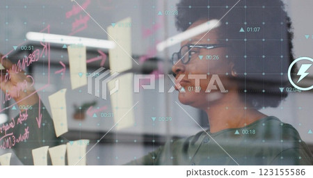 Image of data processing over biracial casual businesswoman taking notes on glass wall 123155586