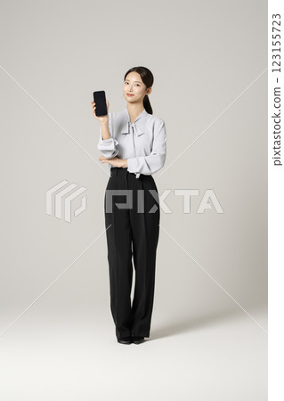 A woman in her 20s wearing a suit standing holding a smartphone 123155723