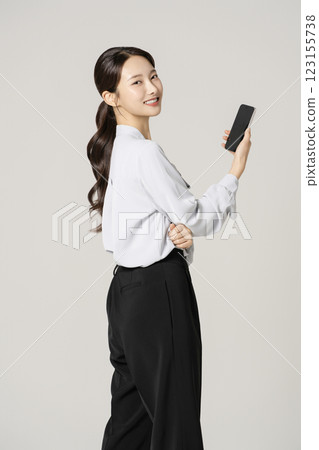 A woman in her 20s wearing a suit standing holding a smartphone A woman in her 20s wearing a suit standing holding a smartphone 123155738