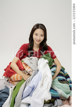 A woman in her 20s buried in a mountain of clothes. 123155864